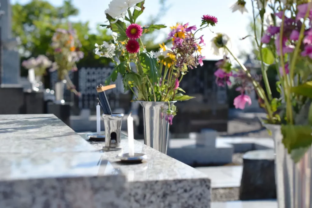 Bouquet de fleurs et bougies déposés sur une tombe en granite dans un cimetière.