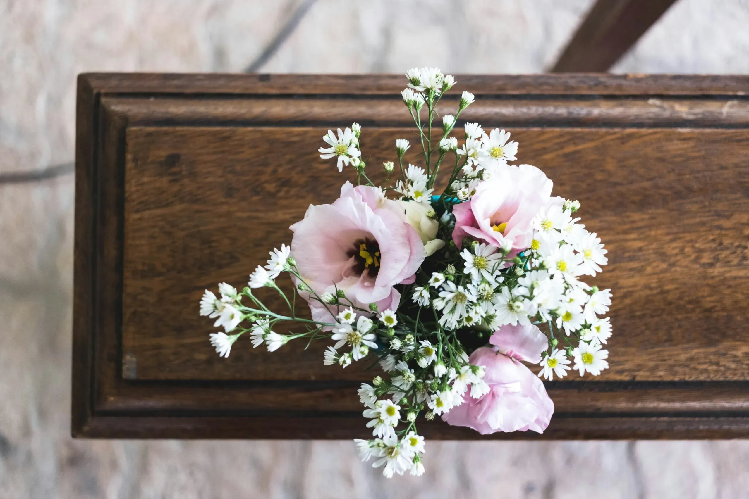 Petit bouquet de fleurs roses et blanches posé sur un cercueil en bois foncé.