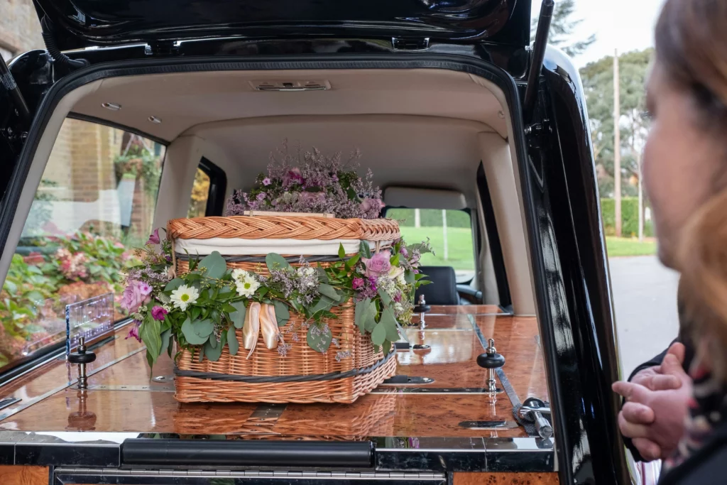 Cercueil en osier tressé orné de fleurs au fond d'un corbillard funéraire.