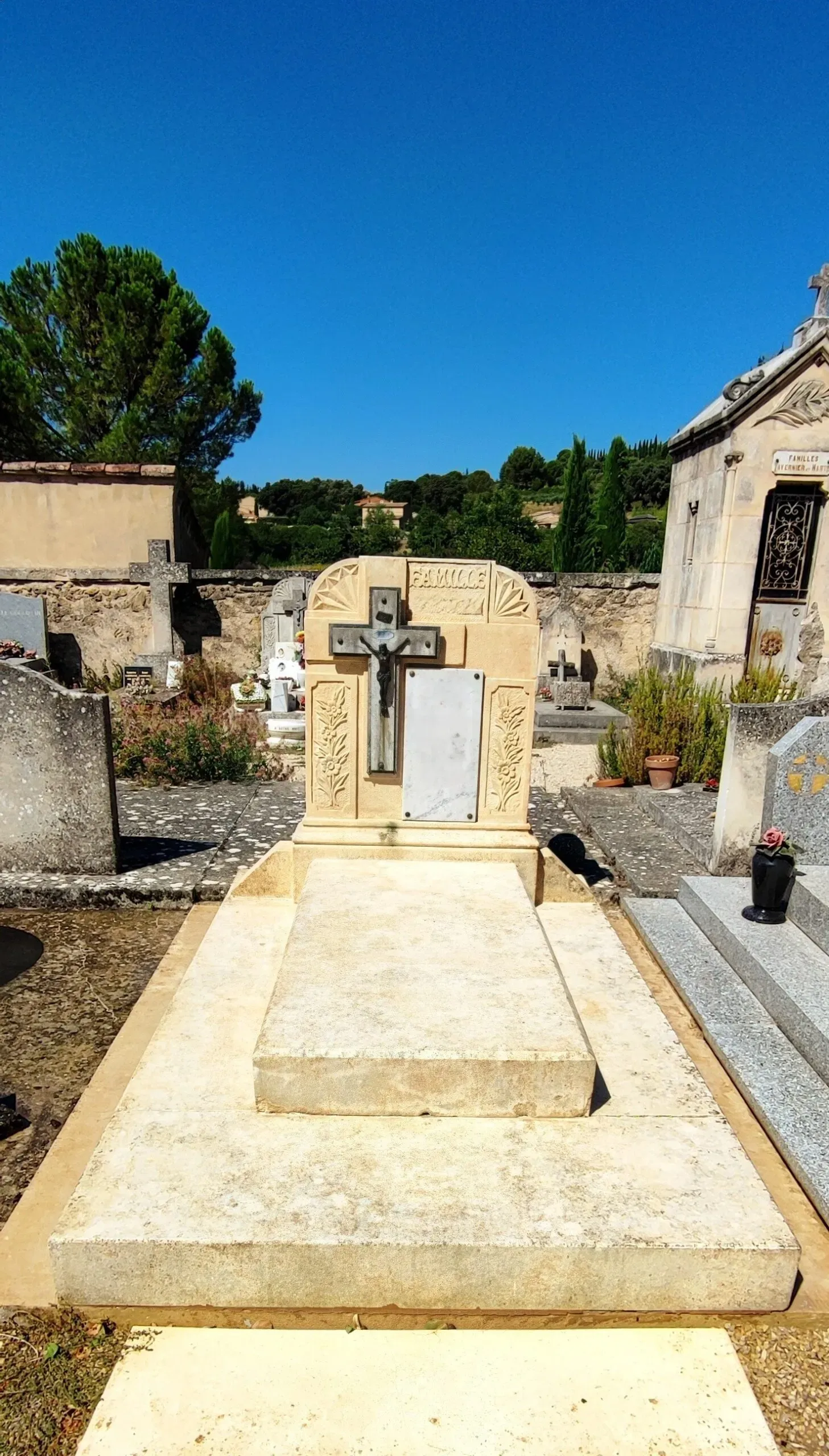 Monument funéraire en pierre claire rénové avec croix noire en cimetière.